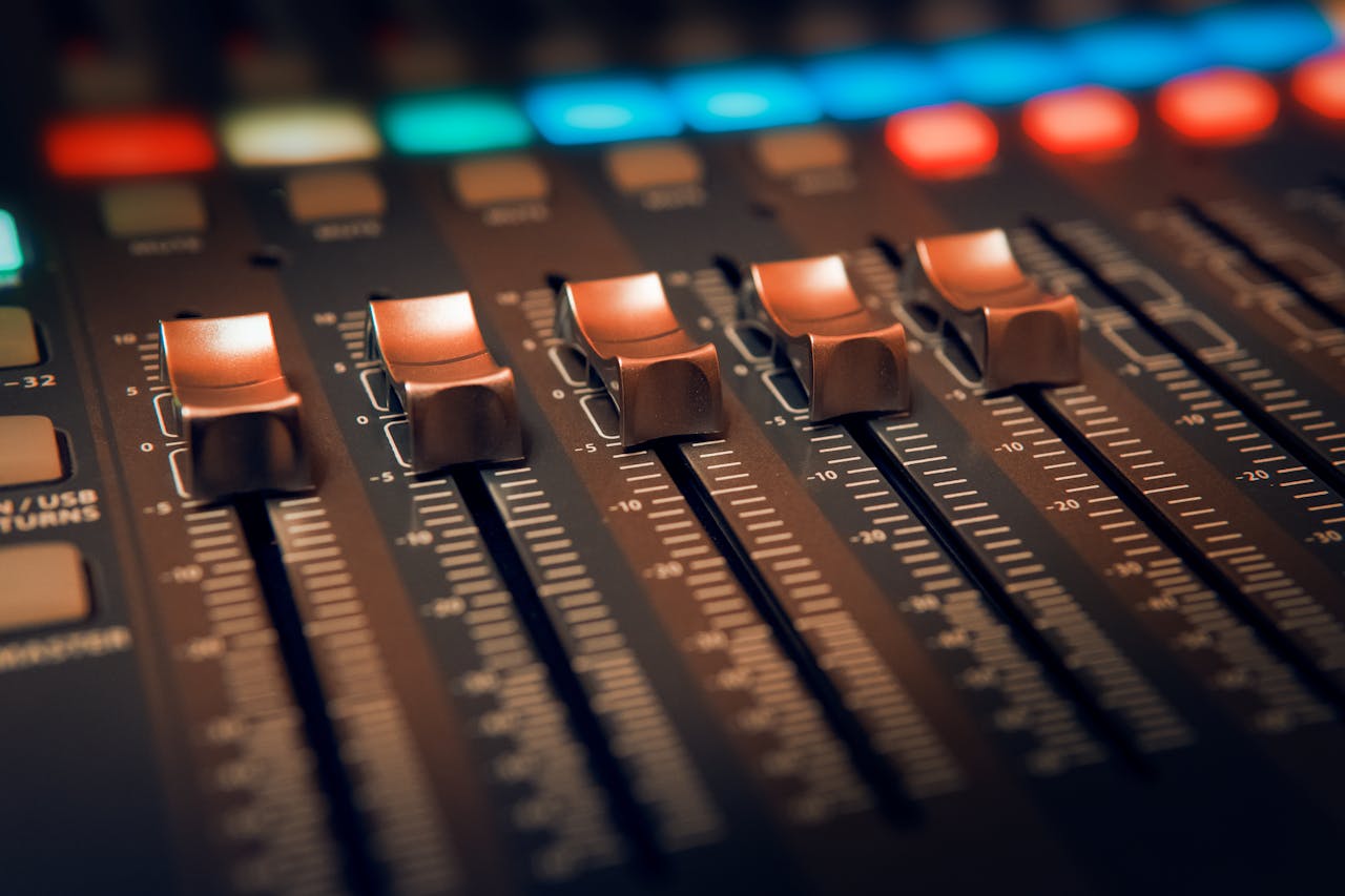 Detailed close-up of an audio mixer with illuminated controls in a studio setting.