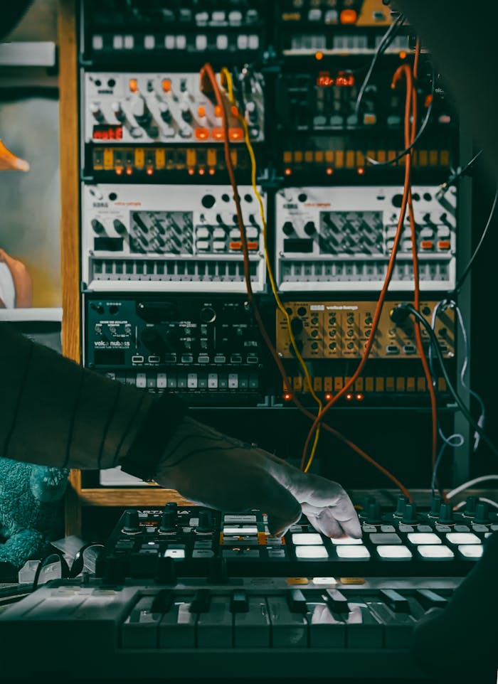 Musician using a synthesizer and controllers in a studio with electronic equipment.